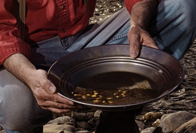 "Old Prospector Panning for gold.  Liquid gold from the sun pouring in over his shoulder from a hot western sunset.  You can see the gold nuggets in his pan.  Striking it Rich!!  Old hat, suspenders, red shirt.  Miners pan, pick ax, and a prospector's dream of a stream to work from."
