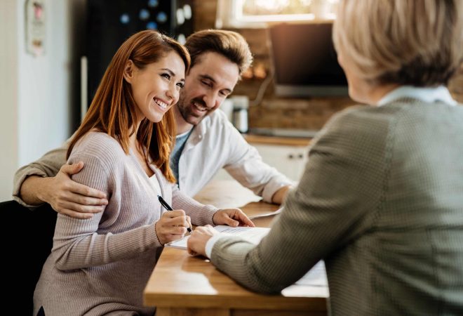 Young happy woman and her husband signing an agreement with insurance agent during a meeting.