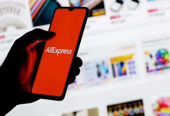 Kazan, Russia - Oct 25, 2021: AliExpress is an Chinese online retail service. A smartphone with the AliExpress logo in a hand on background of the catalog from the site.