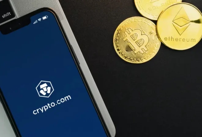 Celular-com-o-logo-da-corretora-Crypto.com-proximo-de-moedas-douradas-do-Bitcoin-e-Ethereum