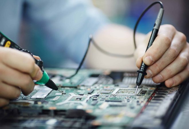 Closeup shot of male hands testing electric current voltage in circuit board of disassembled laptop using multimeter tool on table in maintenance shop