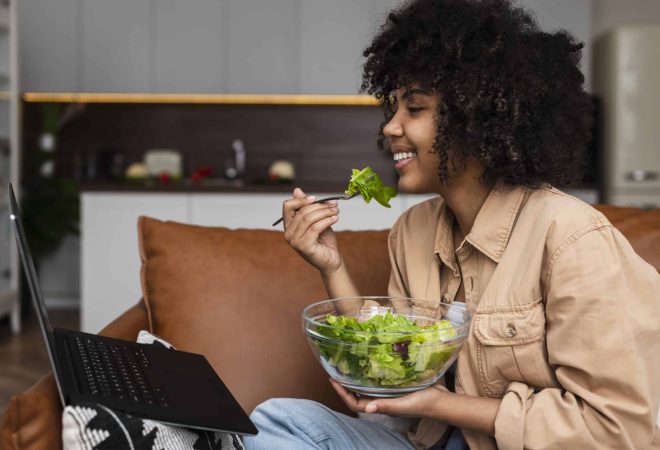 afro-americana-mulher-comendo-salada-e-olhando-no-laptop