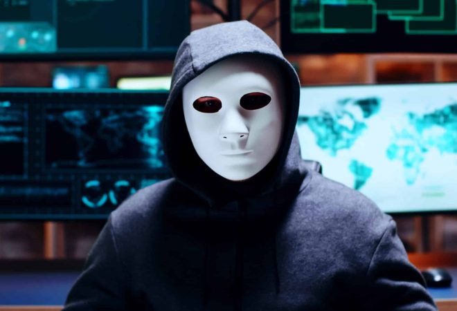 Zoom in shot cyber criminal wearing a white mask looking at the camera.