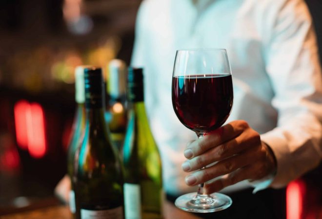 Mid section of bartender holding glass of red wine at bar counter