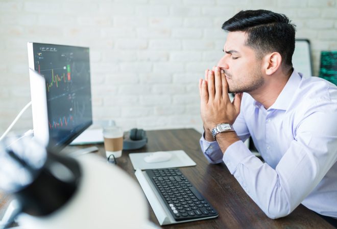 Handsome young Latin finance professional sitting with eyes closed while hoping for good stock trade while working at home