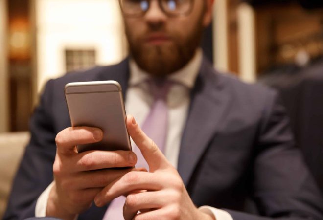 Image of concentrated young bearded businessman sitting indoors and chatting by phone. Focus on phone.