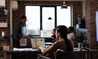 Businesswoman living with disability analyzing report on laptop, working with statistics in disability friendly office. Asian employee suffering from chronic impairment, using wheelchair.