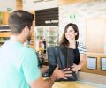Confident female cashier giving bag to young man at checkout counter in supermarket