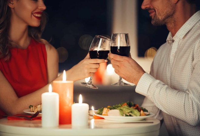 Cropped photo of young lovers having romantic dinner and drinking red wine at home