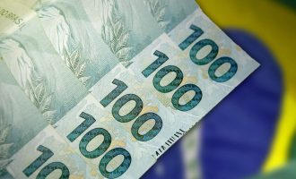 Close up of 100 Real Brazilian banknotes in front of the national flag. Finance and business concept