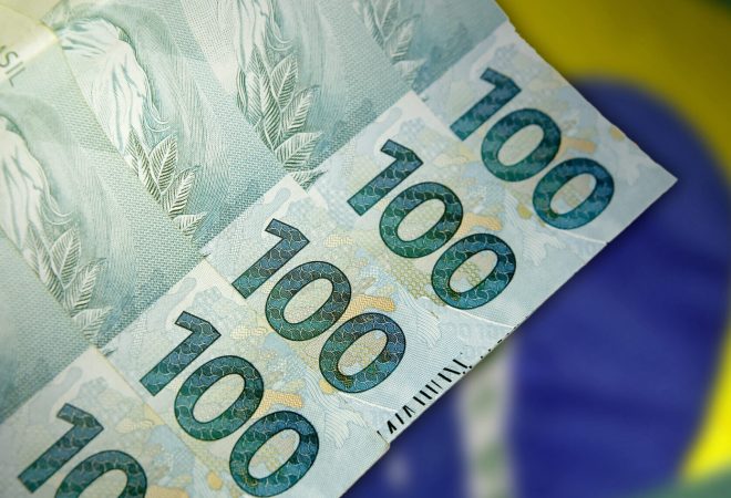 Close up of 100 Real Brazilian banknotes in front of the national flag. Finance and business concept
