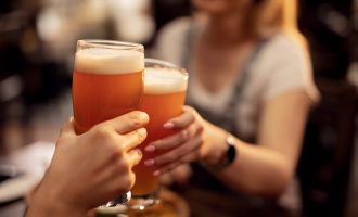 Close up of unrecognizable couple toasting with lager beer in a bar.