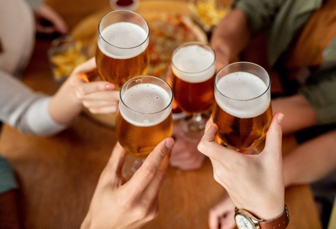 Close-up of friends celebrating and toasting with beer in a pub.