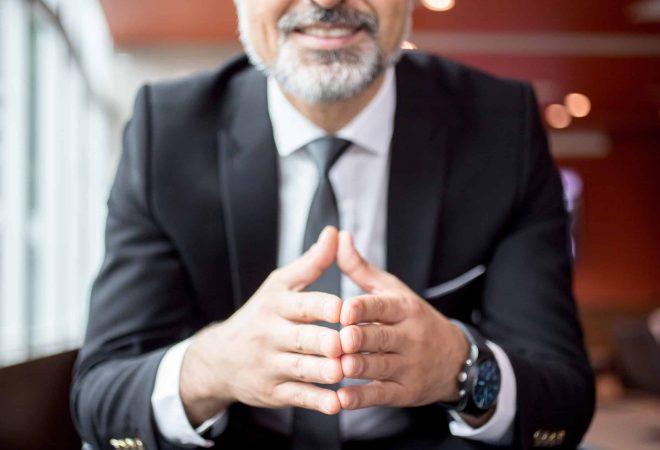 Contemplative smiling businessman reflecting and gesturing. He touching fingers when thinking or taking decision. Body language concept