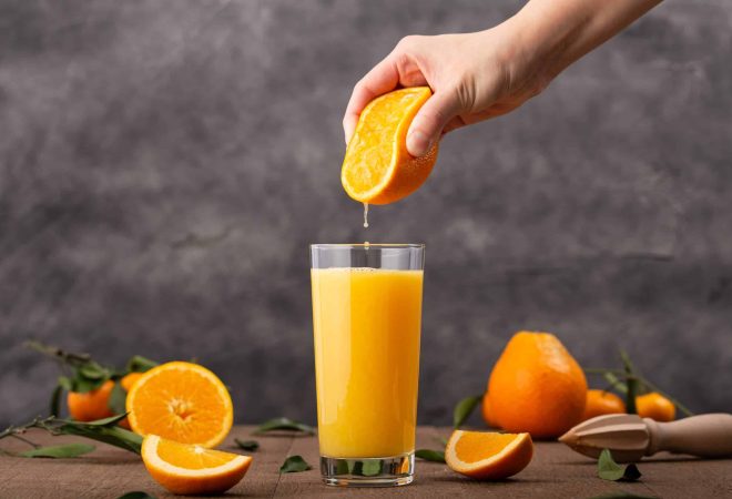A glass of orange juice and a person squeezing an orange in it