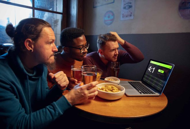 Device screen with application for betting and score. Device with match results on screen, excited fans on background during match. Gambling, betting, sport, finance, modern technologies concept.