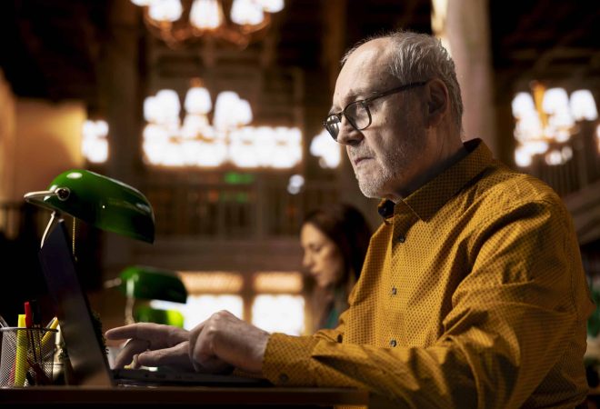 Elderly adult reading complex research documents under a green lamp, showcasing the power of wisdom and focus in senior learning environments. Academic studying in a public library.