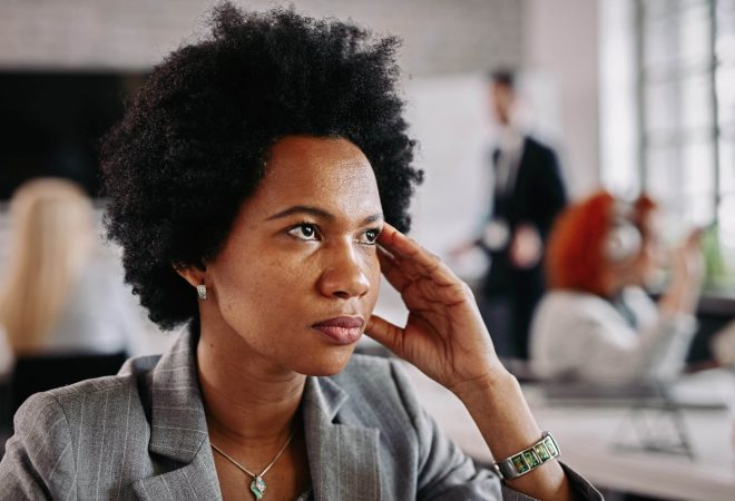 African American businesswoman looking thoughtful while being in the office. There are people in the background.