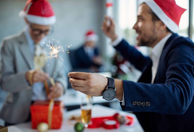 Close-up of businessman having fun with sparkler while celebrating Christmas with colleagues in the office.