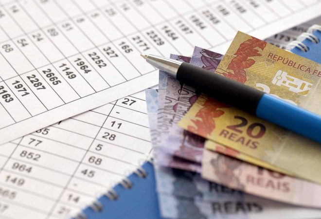 Pen with Brazilian money bills on documents with calculations table. Concept of business, accounting or taxpaying in Brazil