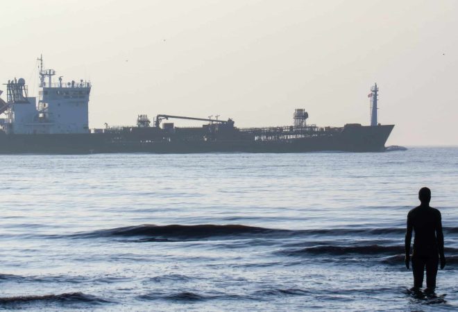 Another Place statue located on the Irish sea coast and floating tanker in Liverpool, United Kingdom