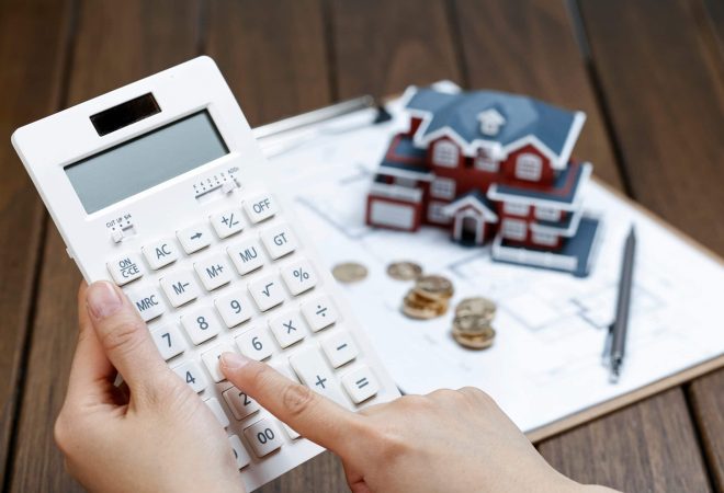 A female hand operating a calculator in front of a Villa house model