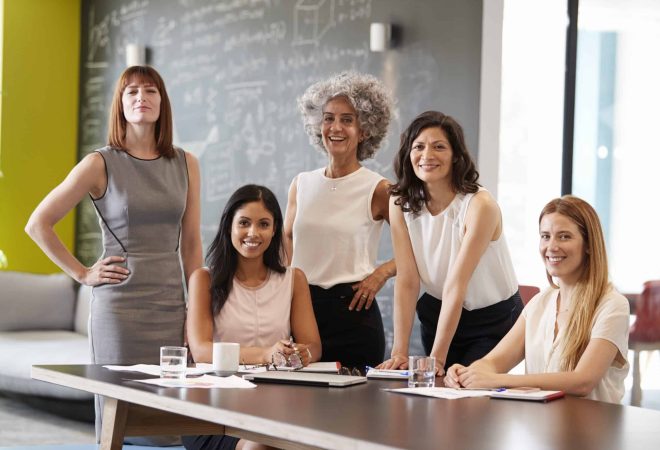 Five female colleagues at a work meeting smiling to camera