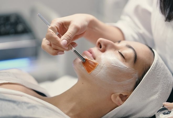 People, beauty, spa, cosmetology and skin care concept - Cosmetologist applying cream on a woman beautiful face with a cosmetologist brush.