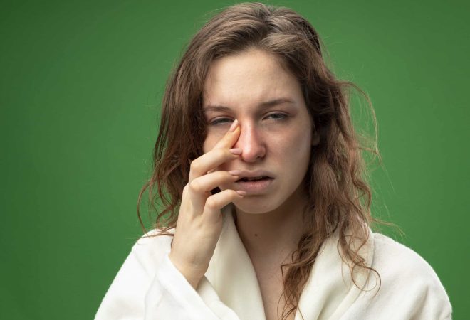 weak young ill girl looking at camera wearing white robe wiping eye with finger isolated on green background