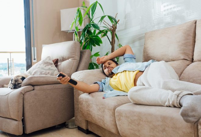 A photo of a handsome Hispanic man lying on a sofa and watching TV
