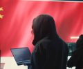 Chinese hacker working in governmental hacking room with Chinese flag on a big screen. Having the mission on inflicting fear and misinformation among the population. Dictatorship propaganda. Camera B.
