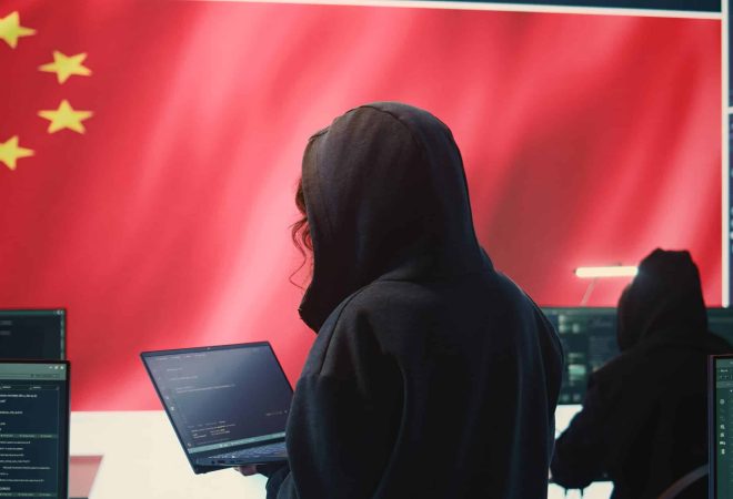 Chinese hacker working in governmental hacking room with Chinese flag on a big screen. Having the mission on inflicting fear and misinformation among the population. Dictatorship propaganda. Camera B.