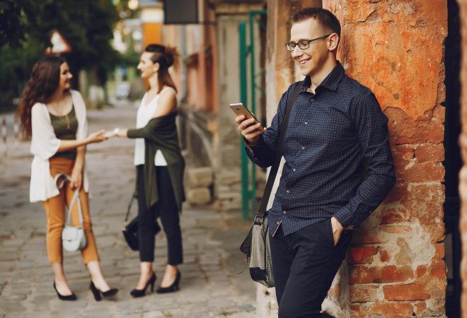 young and handsome guy communicates with his two girlfriends in a sunny city and enjoys the phone