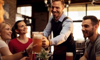 Happy waiter giving beer to his customers while serving them in a bar.