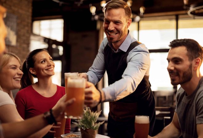 Happy waiter giving beer to his customers while serving them in a bar.