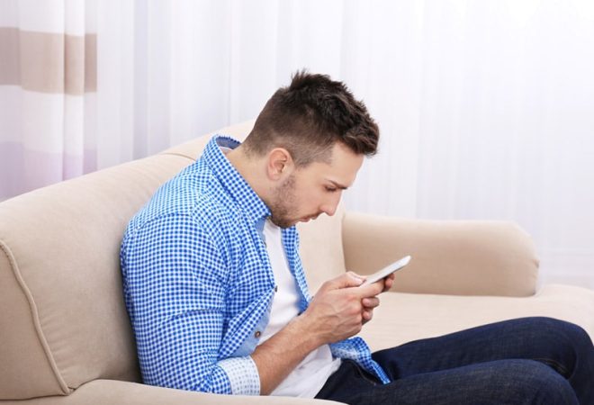 homem-sentado-no-sofa-mexendo-no-celular-com-pescoço-inlinado