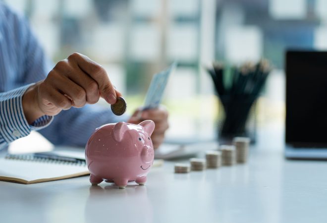 Hands of a young Asian businessman Man putting coins into piggy bank and holding money side by side to save expenses A savings plan that provides enough of his income for payments.