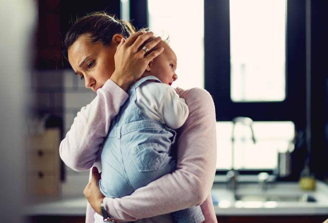 Young worried mother comforting her crying baby at home.