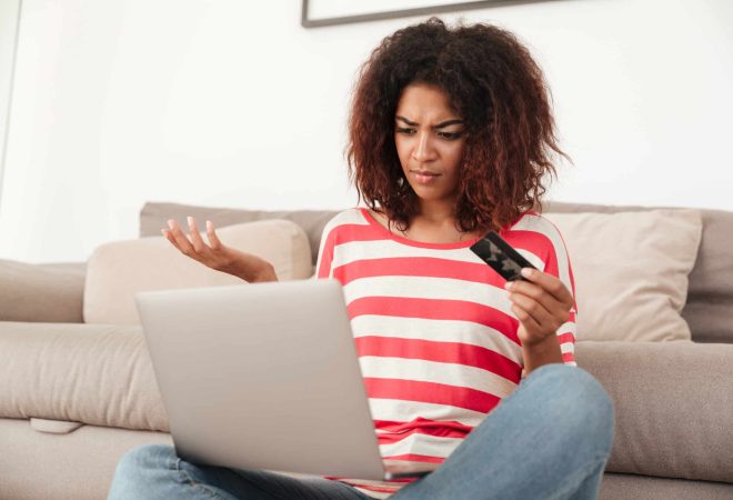 Young confused upset african woman using laptop on sofa at home