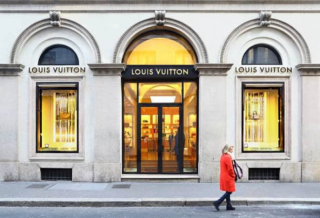 Milan, Italy - February 12, 2015: The entrance and two windows of Louis Vuitton boutique in via Monte Napoleone. A woman is passing in front of it.
