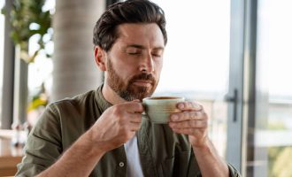 Bearded man closing his eyes and smelling coffee in a cup, enjoying the aroma of the beverage during a break in a cafe