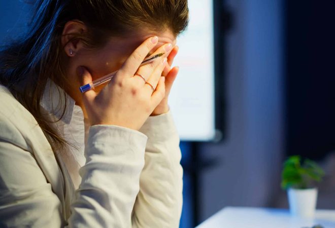 Close up of stressed busy woman with headache working from business office late at night. Tired focused employee using modern technology network wireless doing overtime for job checking reports