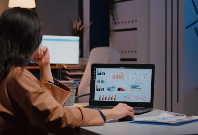 Overworked businesswoman typing financial statistics on laptop sitting at desk table in startup company office late at night. Workaholic entrepreneur planning economic project before company deadline