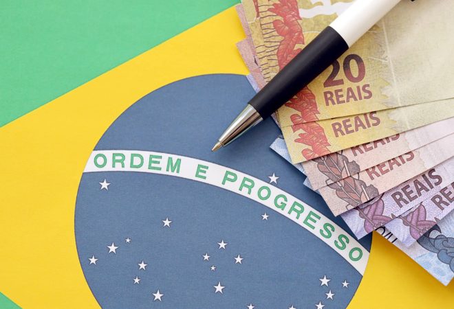 Pen with Brazilian money bills on flag of Brazil republic. Concept of business, accounting or taxpaying in Brazil