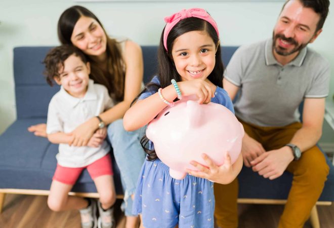 Portrait of a cute little girl putting money on a pink piggy bank to save for a new toy for her and her small brother