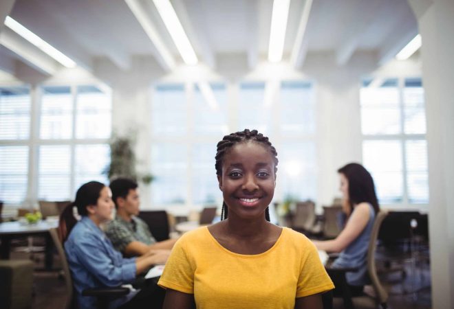 Portrait of woman smiling at camera while colleagues working in background at the office