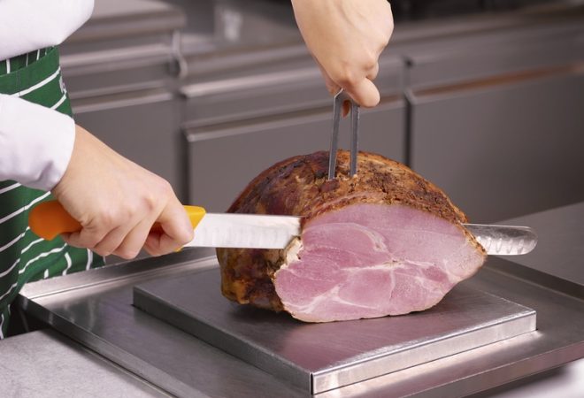 Close up of a chef carving a joint of ham in a professional kitchen
