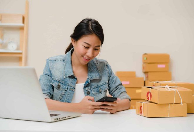 Beautiful smart Asian young entrepreneur business woman owner of SME checking product on stock scan qr code working at home. Small business owner at home office concept.