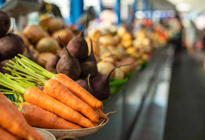 Close-up focused view over organic raw carrots and beetroots sorted in different plates on the counter. Blurred vegetables in the background. Local market.