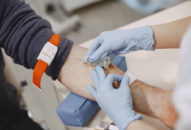 Skillful nurse is doing blood test for man in clinic. Man in a medical mask.